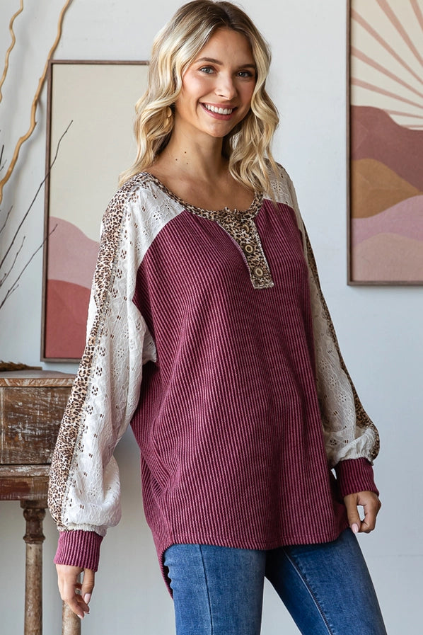 Woman in a burgundy oversized sweater with leopard print sleeves, smiling and posing confidently, paired with denim jeans.