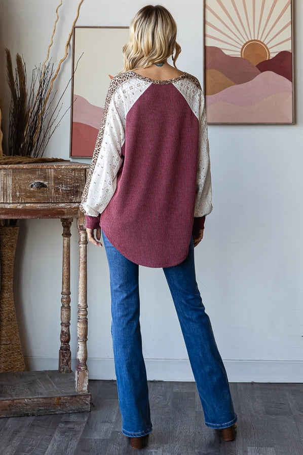 Woman in a burgundy oversized sweater with leopard print sleeves, smiling and posing confidently, paired with denim jeans.