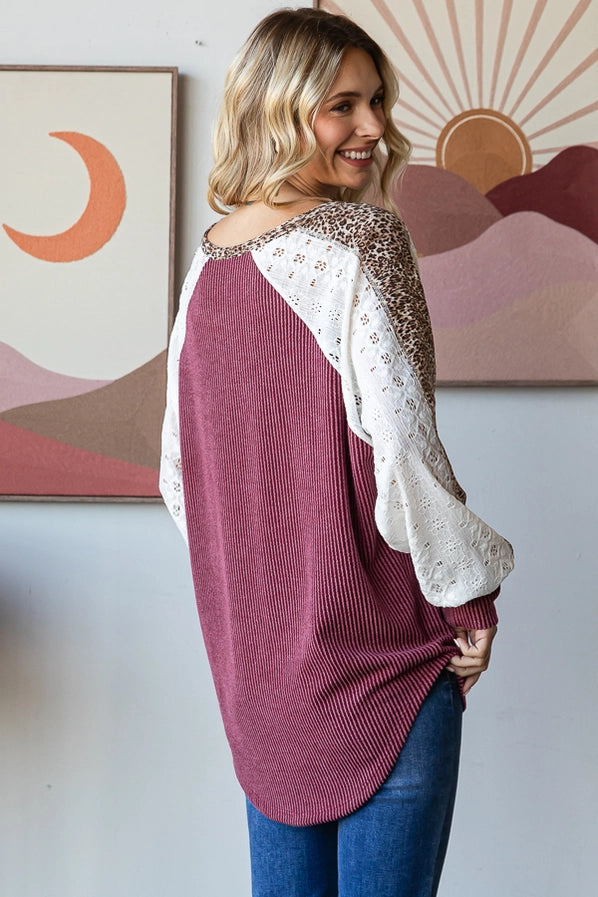 Woman in a burgundy oversized sweater with leopard print sleeves, smiling and posing confidently, paired with denim jeans.
