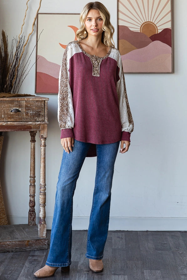 Woman in a burgundy oversized sweater with leopard print sleeves, smiling and posing confidently, paired with denim jeans.