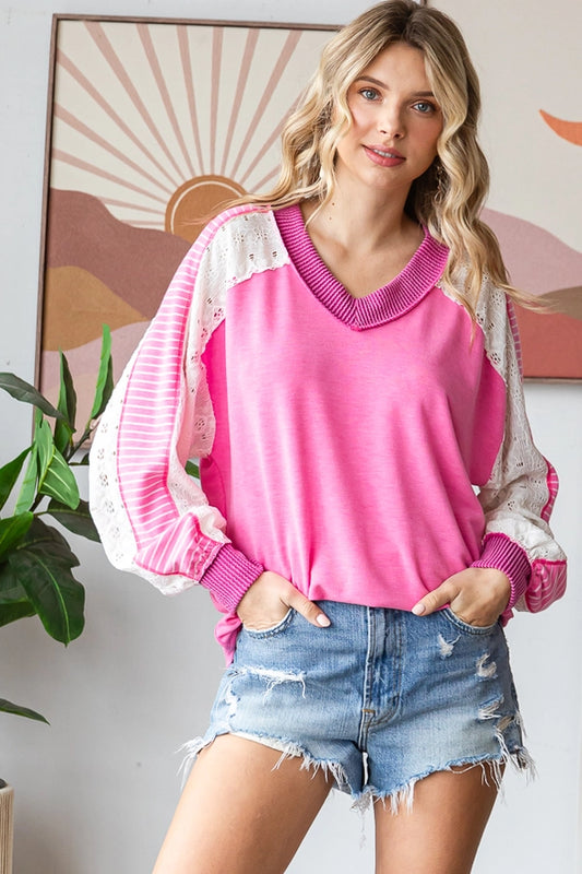 Woman wearing a Color Block V Neck Bishop Sleeve Pullover in pink with striped sleeves, paired with denim shorts, smiling and posing confidently.