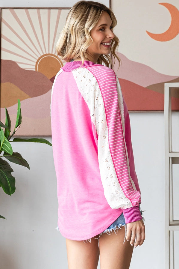 Woman wearing a Color Block V Neck Bishop Sleeve Pullover in pink with striped sleeves, paired with denim shorts, smiling and posing confidently.